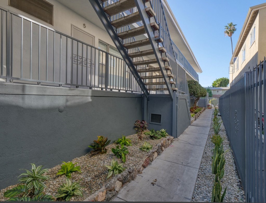 the side of an apartment building with a sidewalk and plants