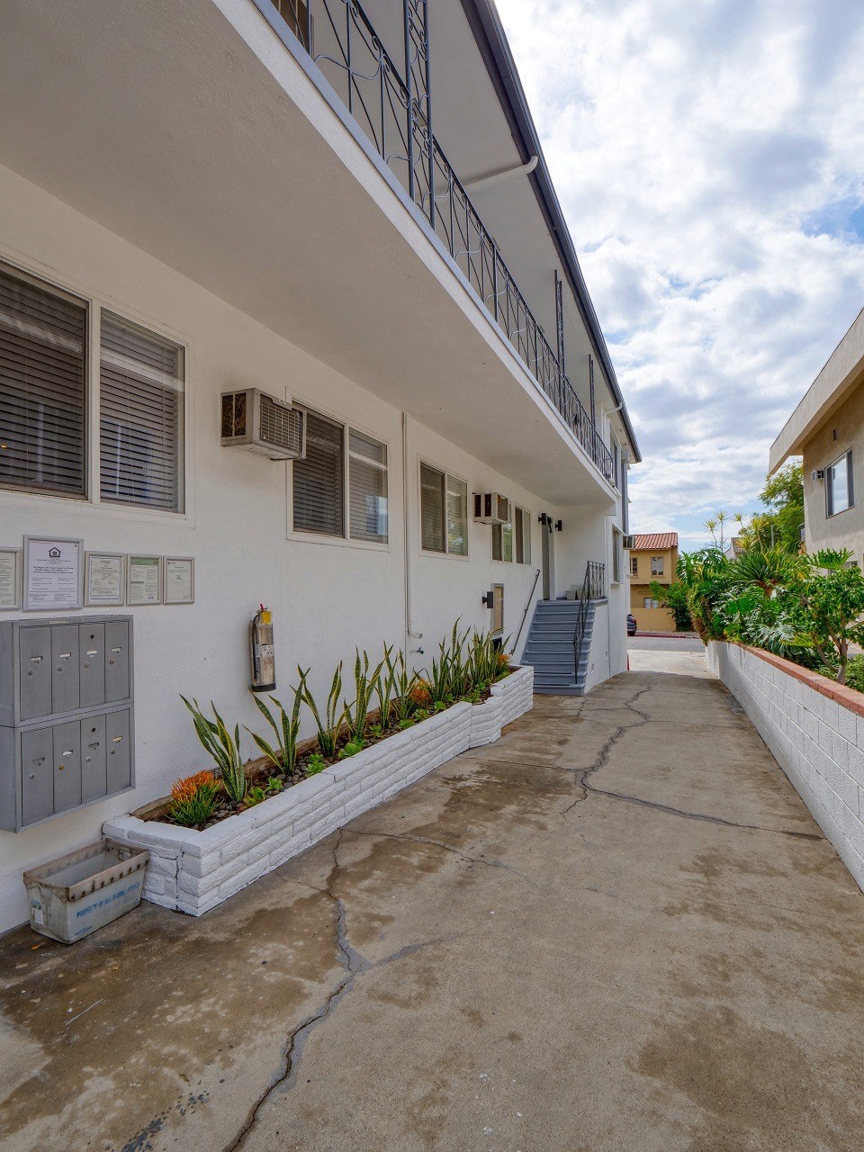 the side of a building with a sidewalk and plants in front of it