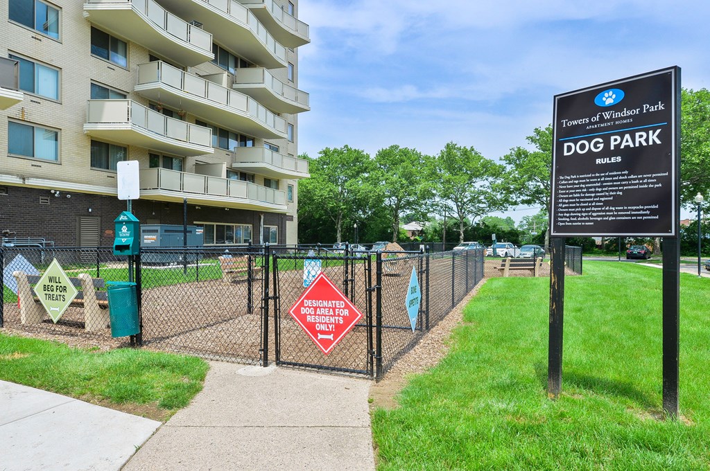 A sign for a dog park is in front of a tall building.