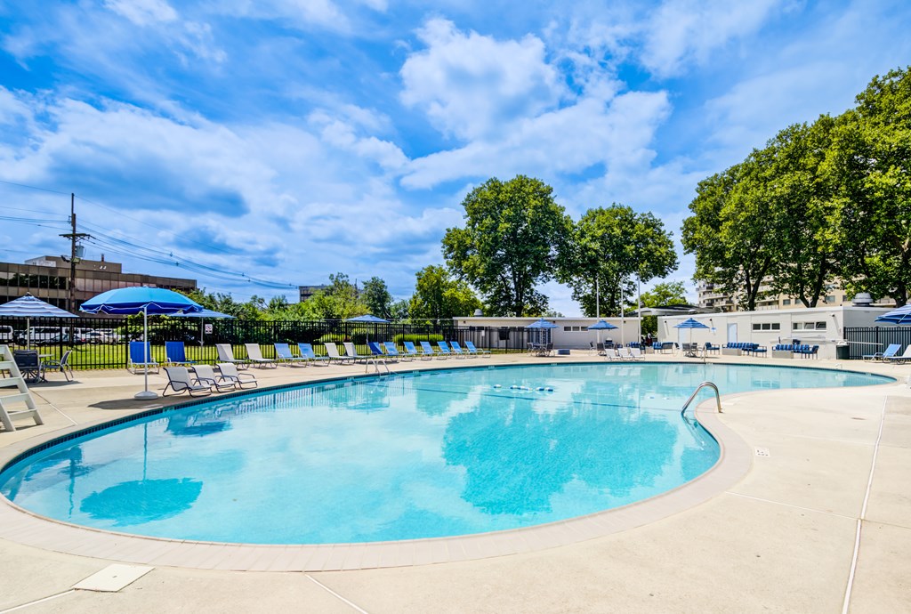 A large outdoor swimming pool with sun loungers and trees in the background.