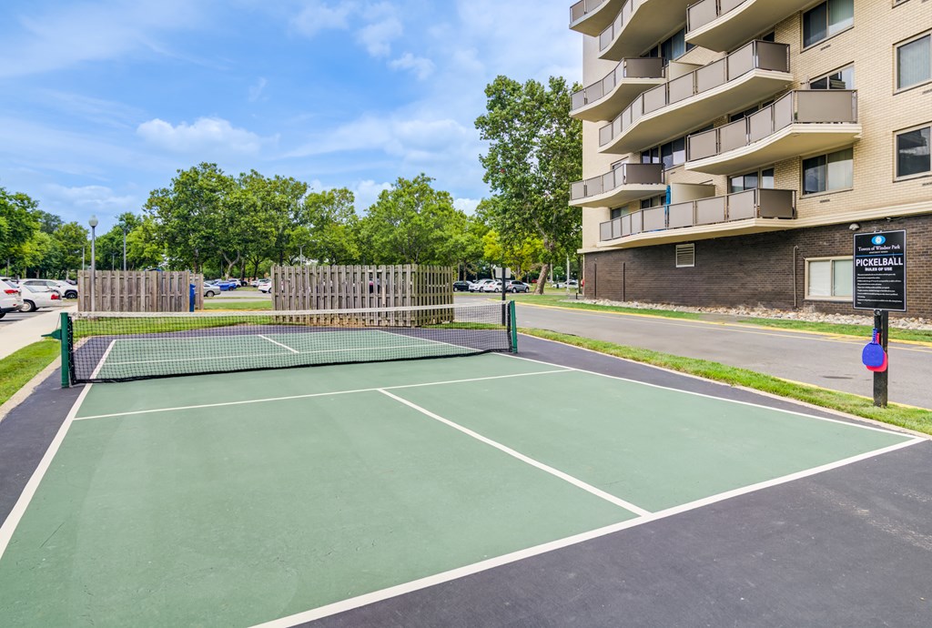 A tennis court is surrounded by a fence and a building.