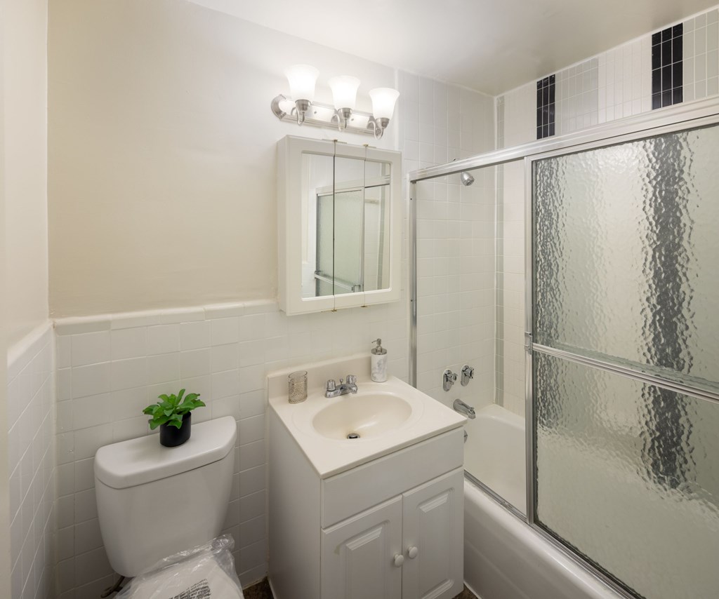 A white bathroom with a toilet, sink, mirror, and shower.