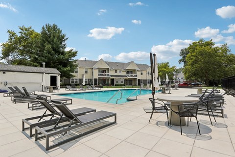 A pool with sun loungers and a table with chairs.
