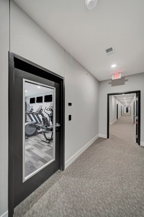 a hallway with a door to a gym with a mirror on the wall