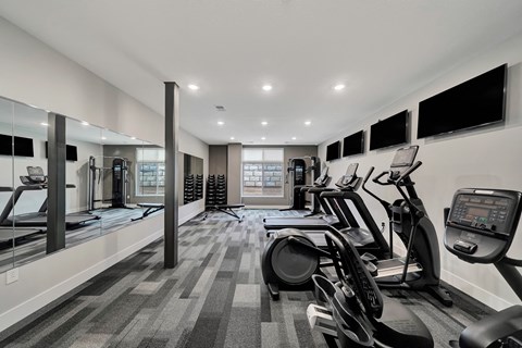 a gym with cardio machines and televisions on the wall