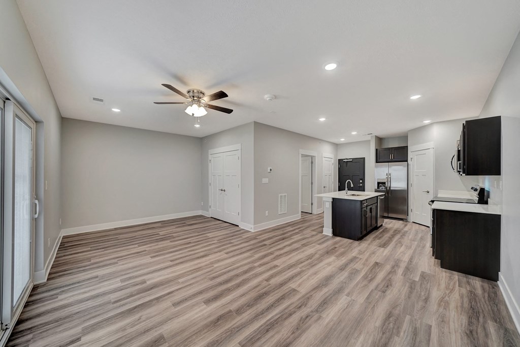 an empty living room with a ceiling fan and a kitchen