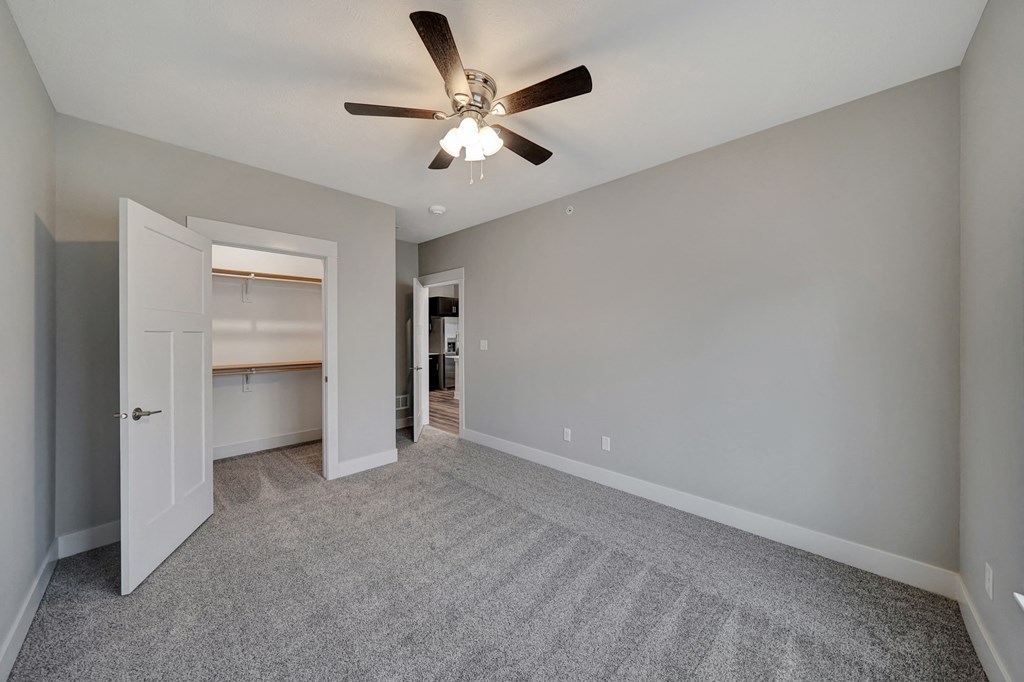 an empty living room with a ceiling fan and a door to a kitchen