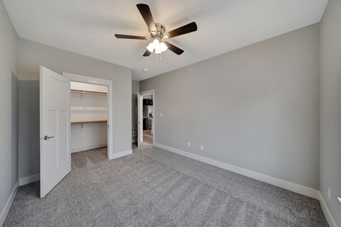 an empty living room with a ceiling fan and a door to a kitchen
