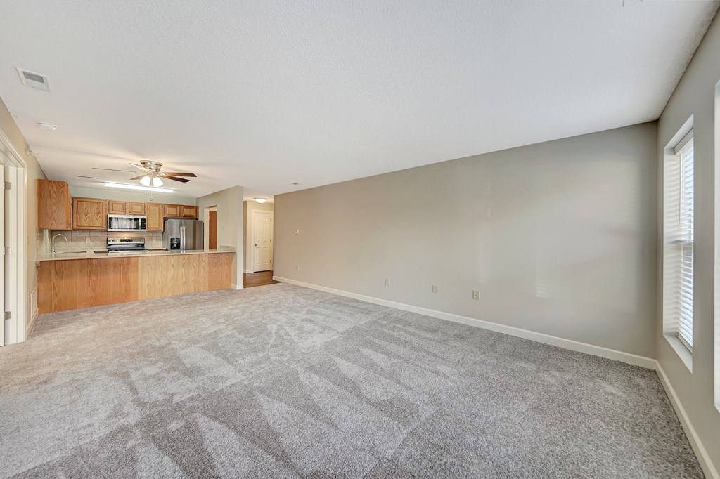 an empty living room with a kitchen in the background