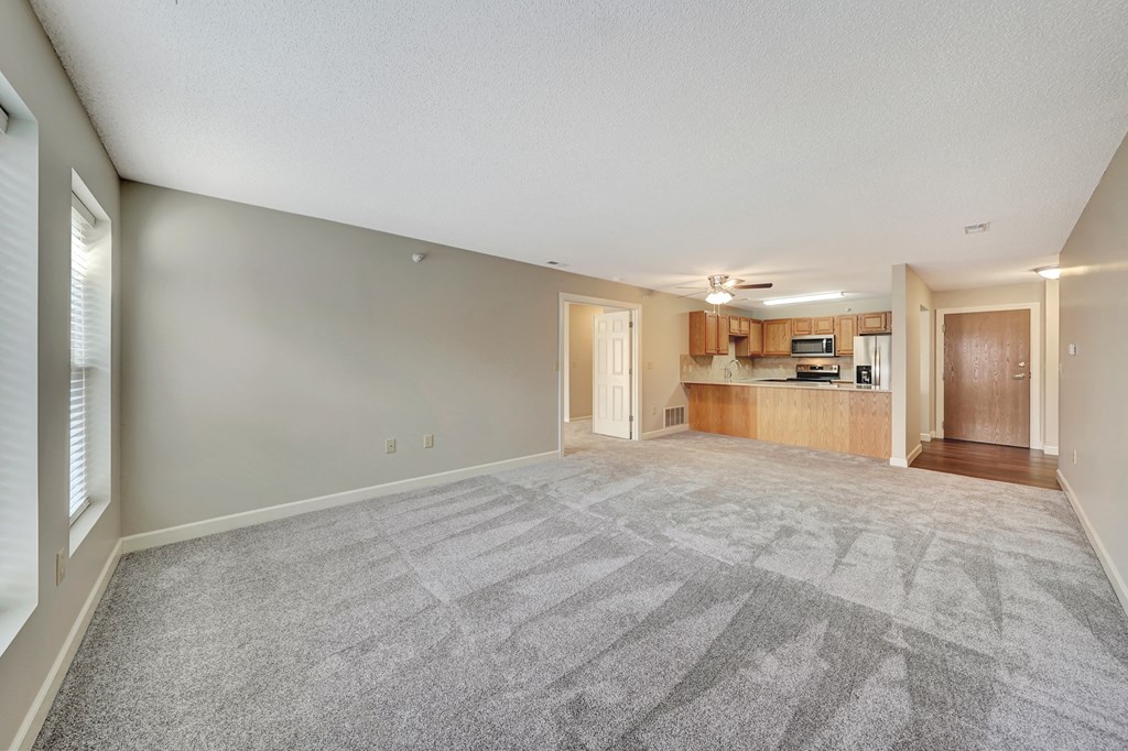 an empty living room with a kitchen in the background