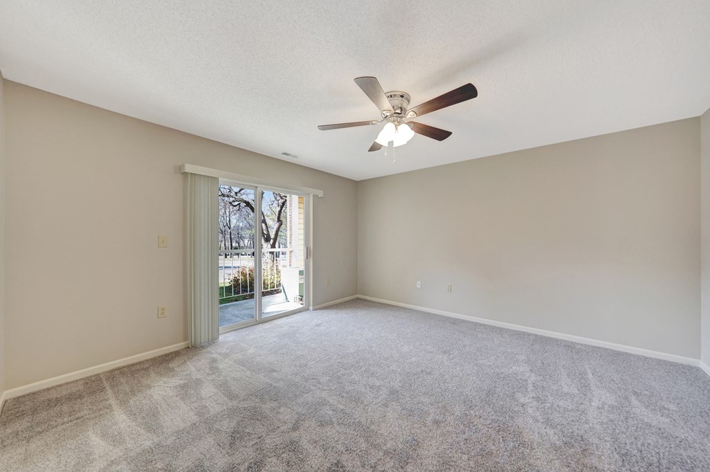 an empty living room with a ceiling fan and a door to a patio