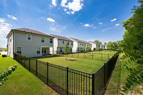 A black fence surrounds a grassy area in front of a row of houses.