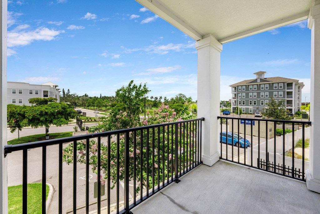 A balcony with a black railing overlooks a parking lot and buildings.