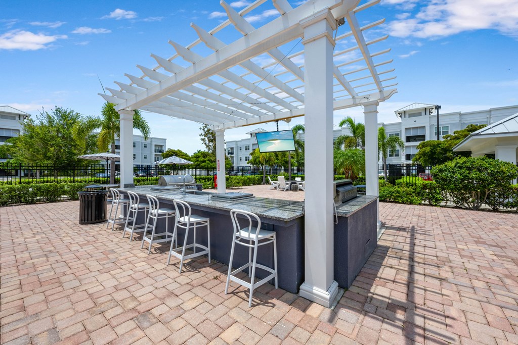 A white pergola is over a bar with stools.