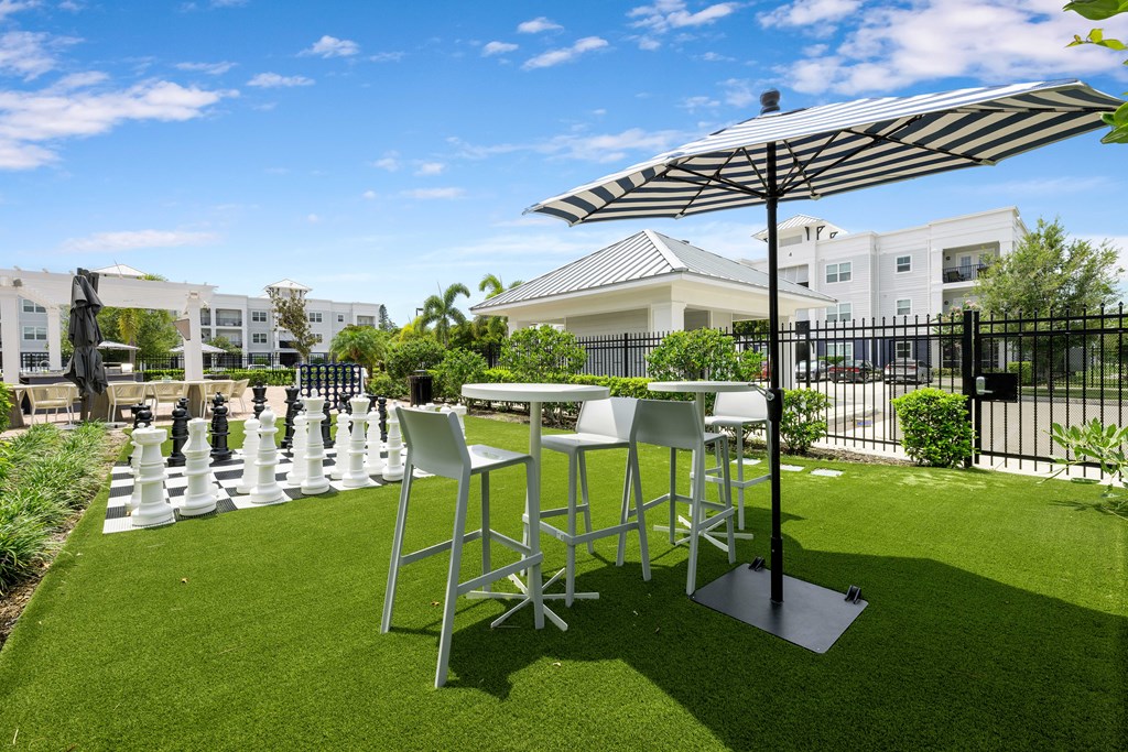 A table and chairs set up on a lawn with a chess board in the middle.