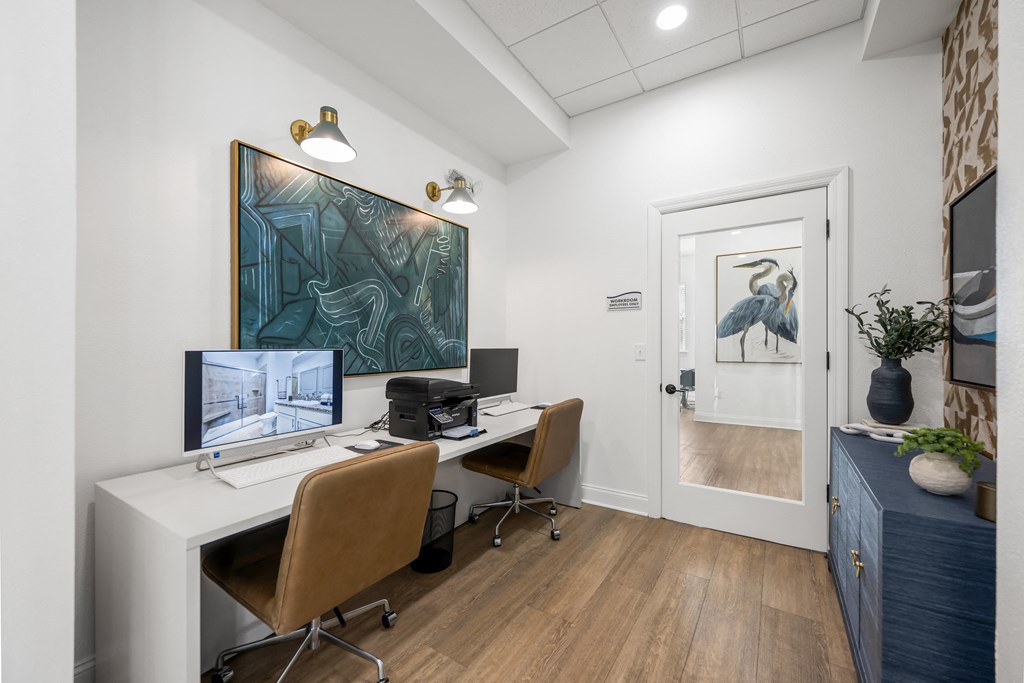A room with a desk, chairs, and a painting on the wall.