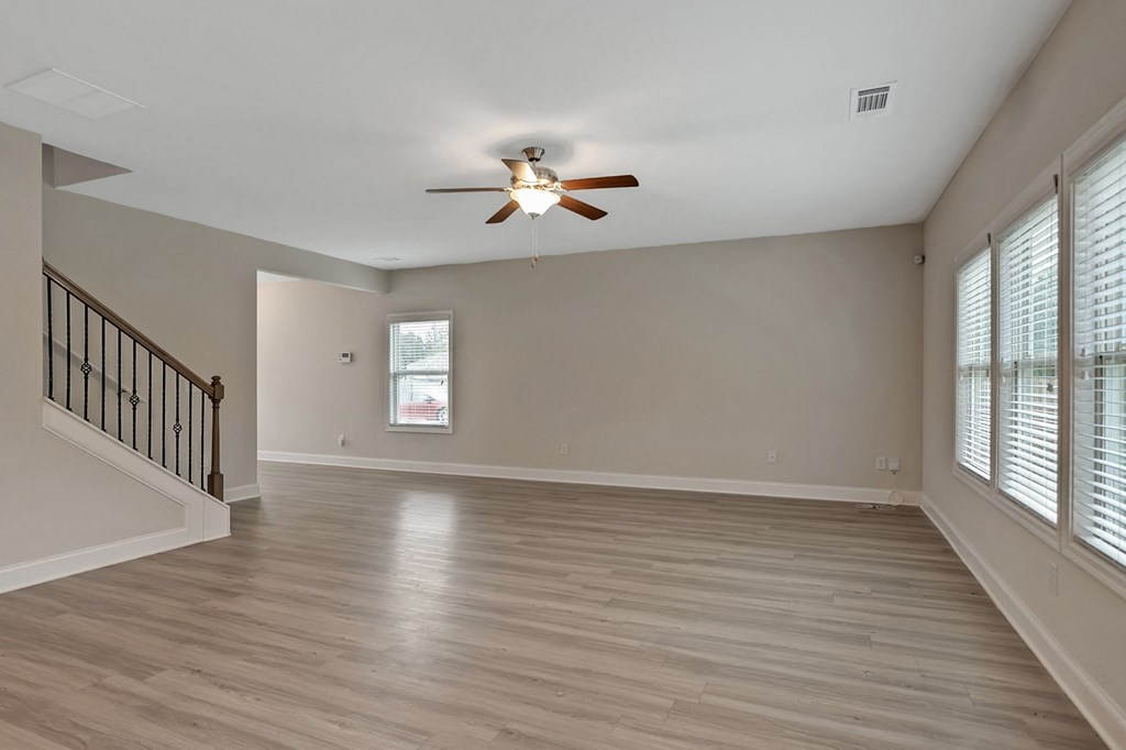 an empty living room with a ceiling fan and windows