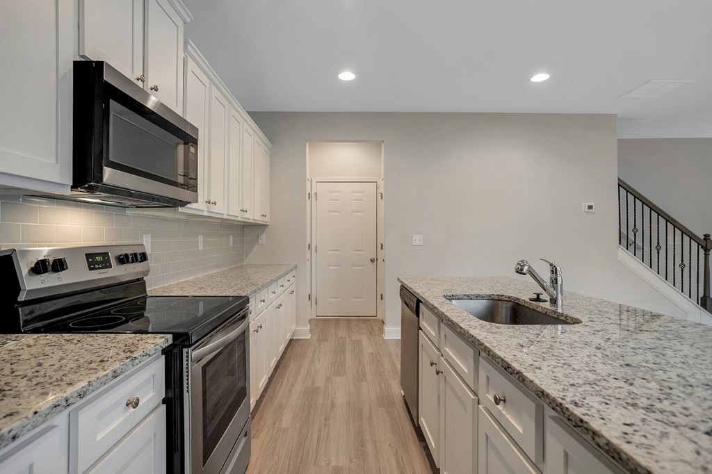 an empty kitchen with granite counter tops and white cabinets