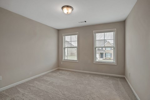 an empty bedroom with two windows and a carpeted floor