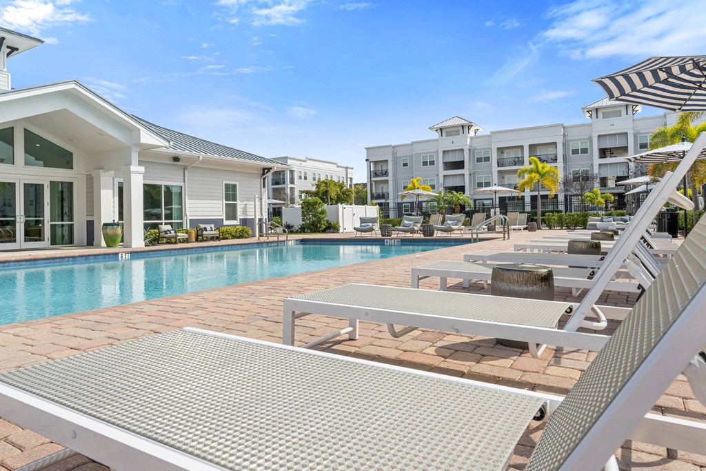 A sunny day at the poolside with a white building and a striped umbrella.