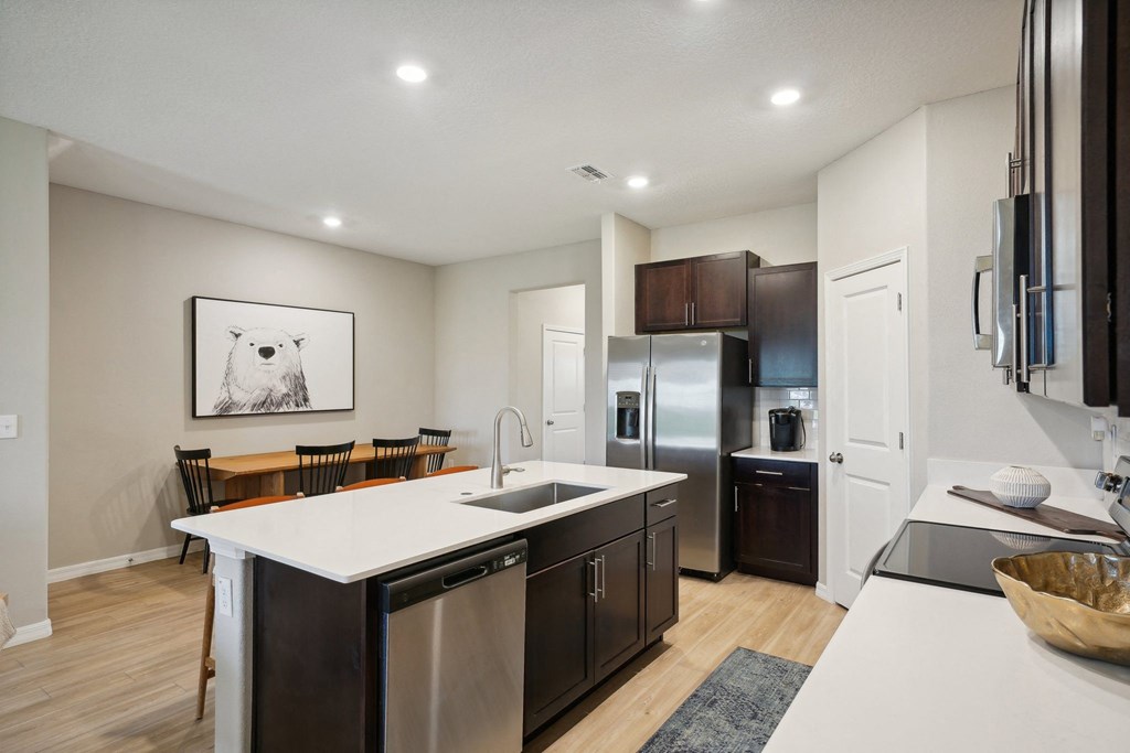 an open kitchen and dining room with a white counter top and a stainless steel refrigerator