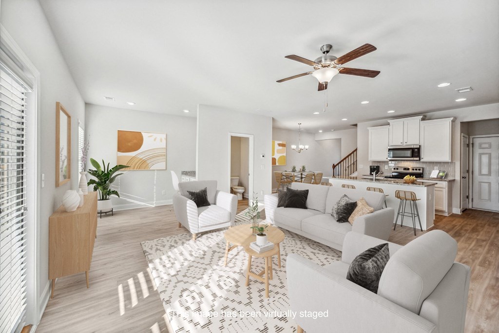 a living room with couches and chairs and a kitchen and a ceiling fan