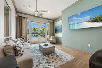 A living room with a couch, a rug, and a television displaying a beach scene.