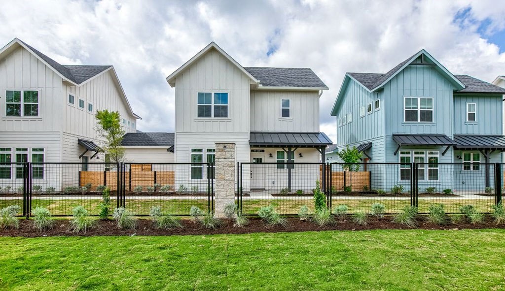 a row of houses with a fence in front of a green field