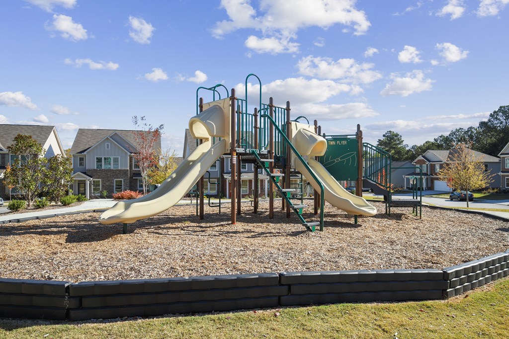 a playground with slides at a park with houses in the background