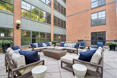 A patio with couches and tables is surrounded by brick buildings.