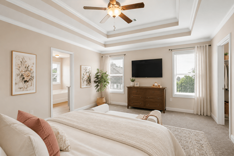 Another perspective view of the serene primary suite, showcasing a modern ceiling fan, sleek entertainment, and sunlit window views.