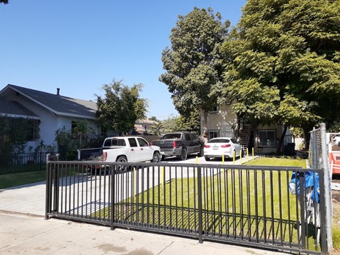 A black metal fence in front of a house with a white car and a grey suv parked behind it.