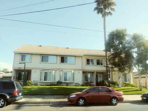 A red car is parked in front of a two-story house.