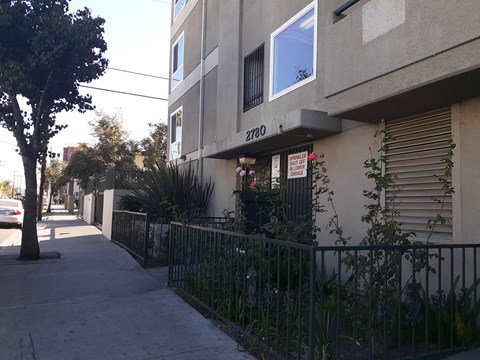 the side of an apartment building with a sidewalk and a fence