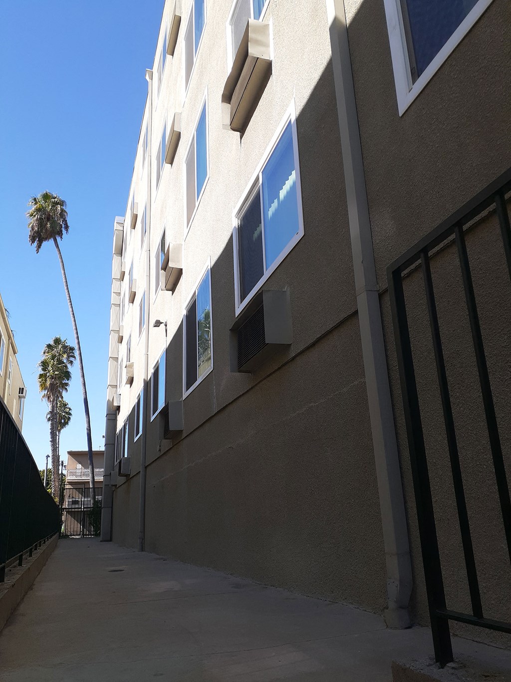 the side of a building with a sidewalk and palm trees