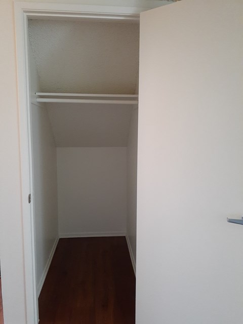 A white closet with a shelf and a door.