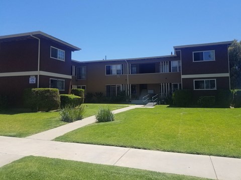 A building with a brown and beige exterior is surrounded by a green lawn and a clear blue sky.