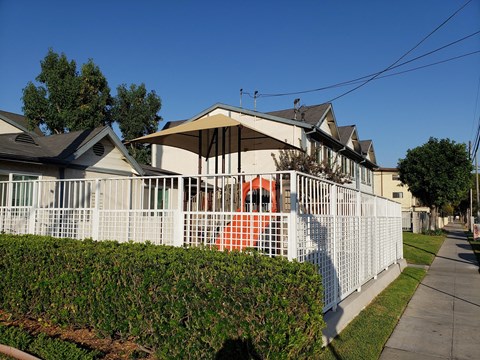 A white fence surrounds a house with a red object in the front yard.
