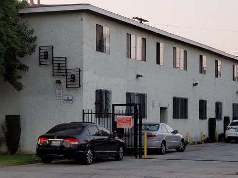 A black car is parked in front of a white building with a gate.