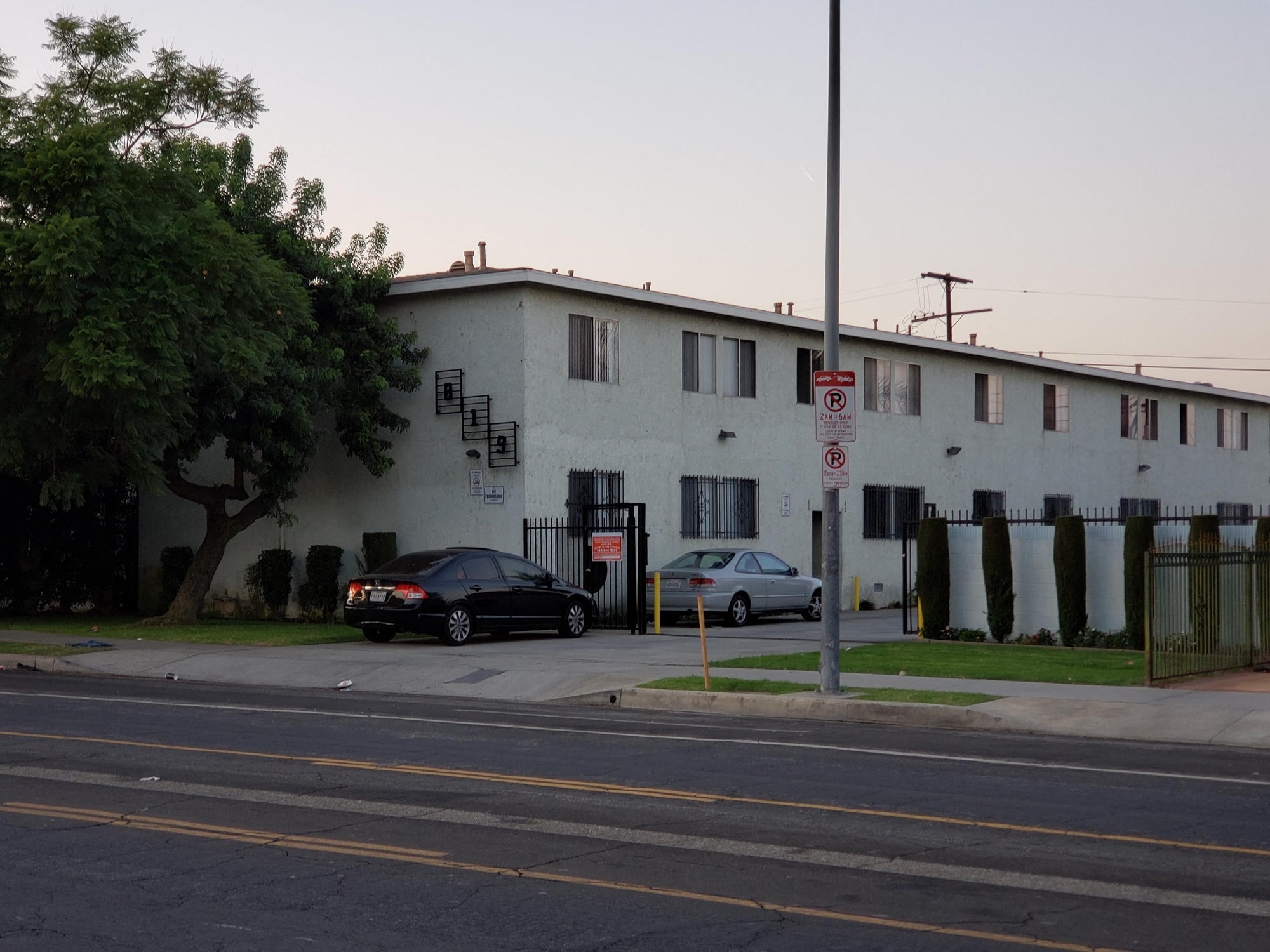 A black car is parked in front of a white building with a no parking sign.
