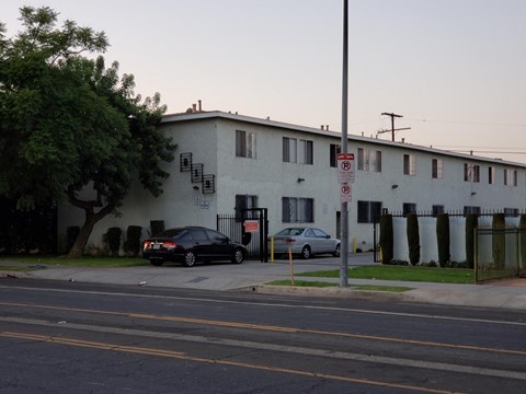 A black car is parked in front of a white building with a no parking sign.