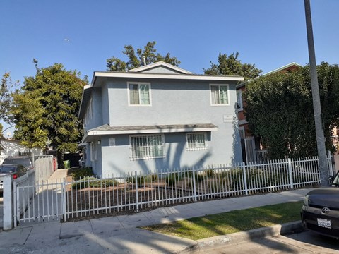 A house with a grey facade is surrounded by a white fence.
