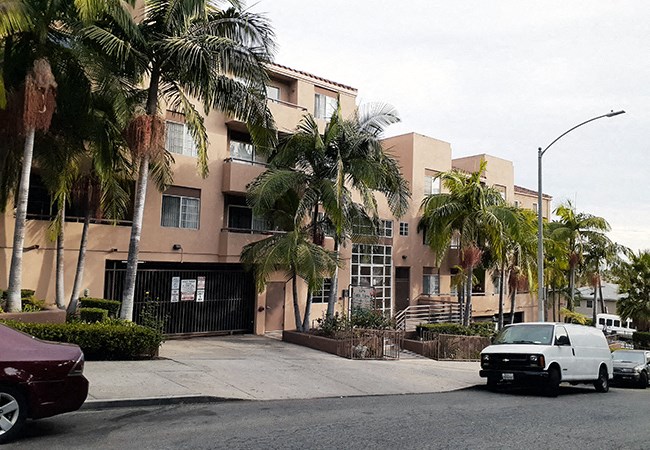 an apartment building with palm trees and cars parked in front
