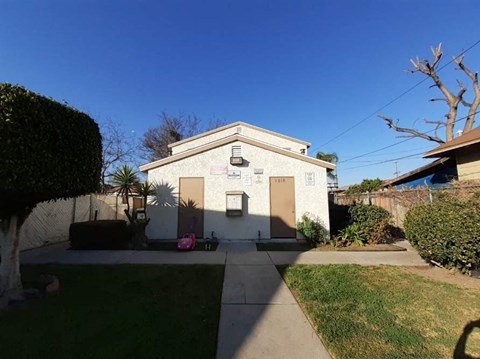 A small building with a sign on it is surrounded by a green lawn and trees.