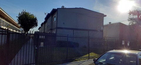 A car is parked in front of a house with a black fence.