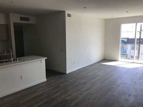 an empty living room with a kitchen and a balcony