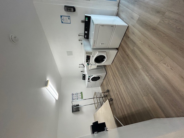 A white washing machine is on top of a wooden floor.