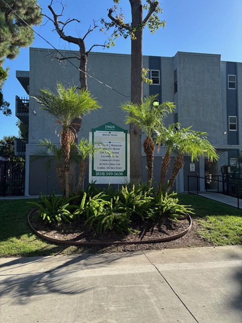 A sign in front of a building with trees and plants.