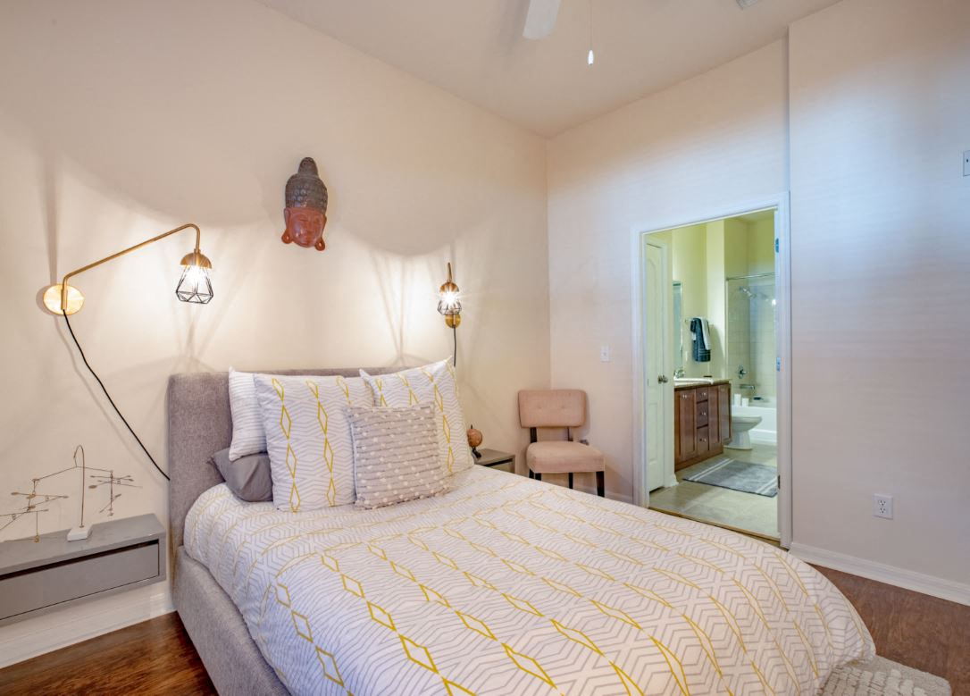 2nd bedroom pictured with accent chair and 1 night stand. Bathroom entry on the right side at The Bartram Apartments in Gainesville, FL 32608