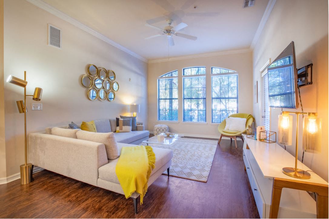 Living room space with dark brown vinyl wood floors and L shaped couch and TV mounted on the right side of the wall at The Bartram Apartments in Gainesville, FL 32608
